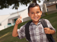 Kindergarten boy wearing a backpack giving a thumbs-up