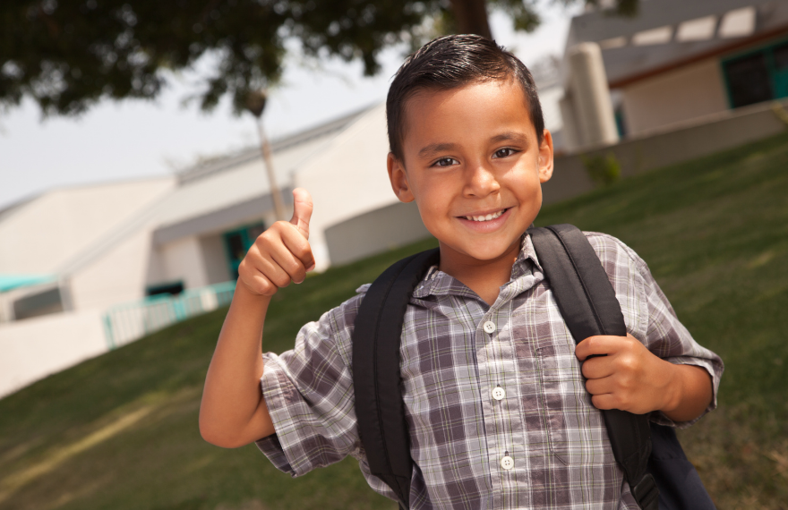 Kindergarten boy wearing a backpack giving a thumbs-up